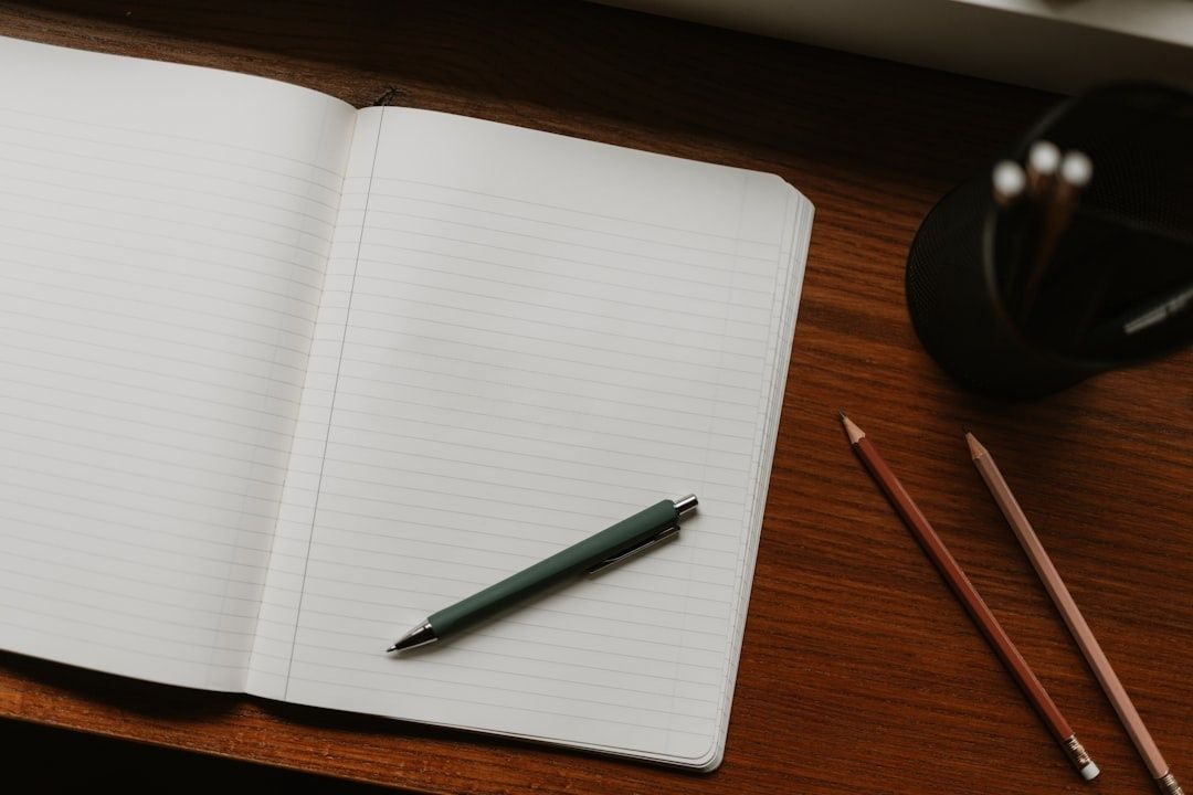 Open gelinieerd notitieboek met pen en potloden op een houten bureau