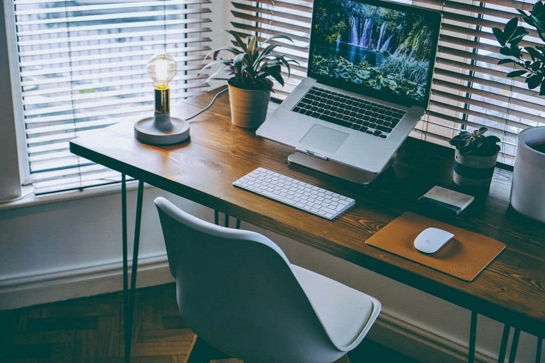 Bureau met laptop naast een raam met jaloezieën en planten