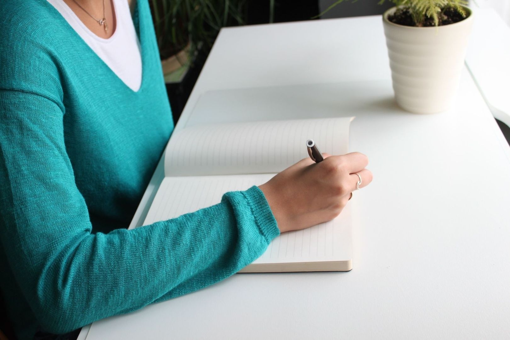 Persoon schrijft met een pen in een gelinieerd notitieboek aan een bureau
